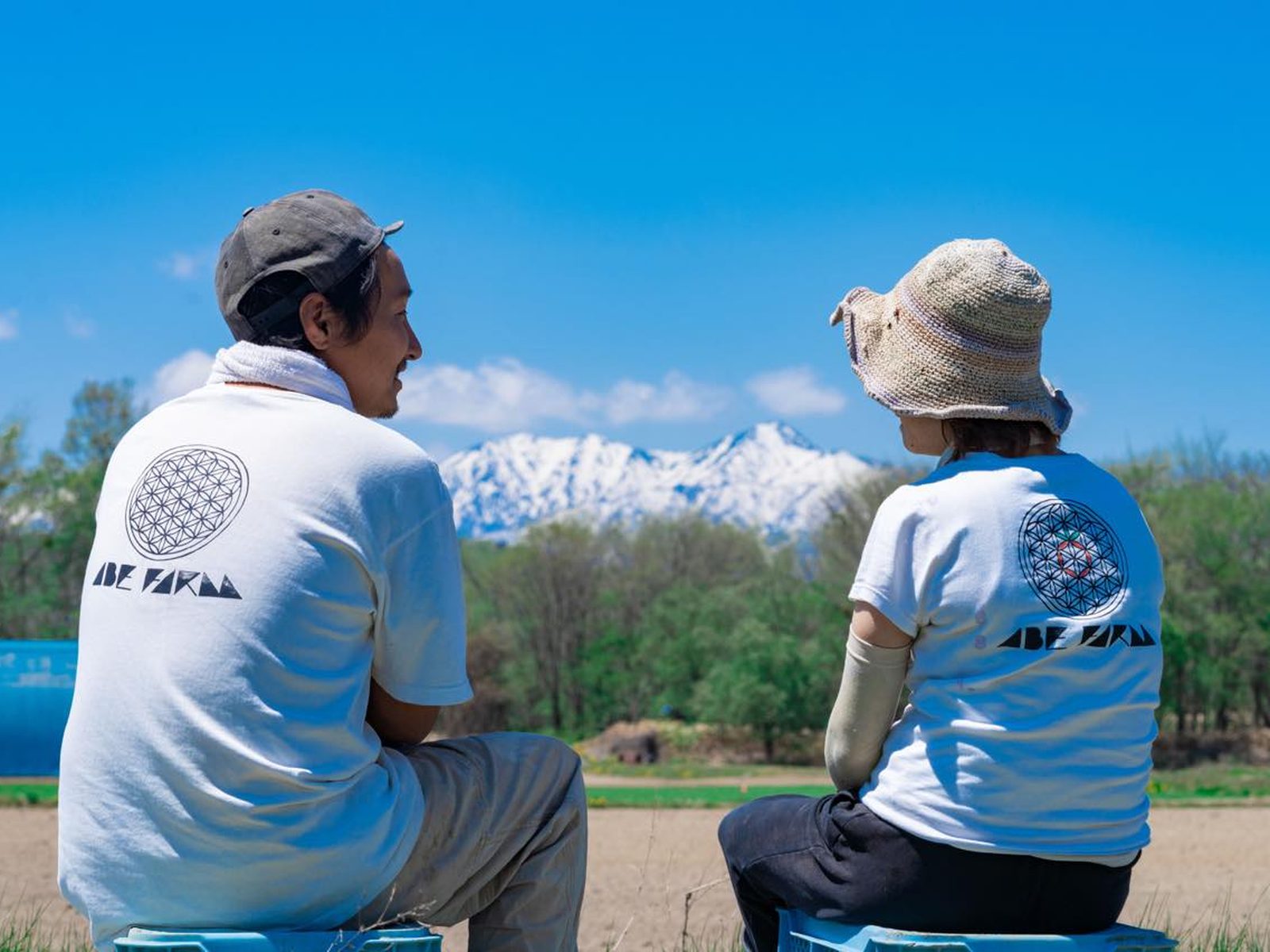 農園のTシャツを着て畑から山並みを眺める阿部さんご夫婦